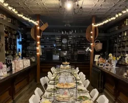 A long, formally set dining table inside a cozy, dimly lit room with wooden floor.