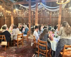 A group of people dining and socializing at tables inside a rustic, barn-like event space.
